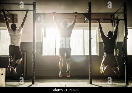 Three men doing pull ups on exercise bar in gymnasium Stock Photo