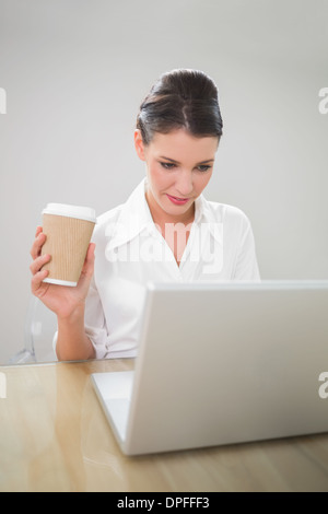 Focused gorgeous businesswoman holding coffee while using laptop Stock Photo