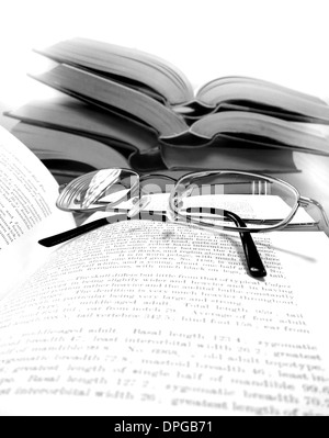 Stack of old books on a desk or table in a library with reading glasses Stock Photo
