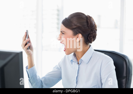 Angry classy brown haired businesswoman shouting at her mobile phone Stock Photo