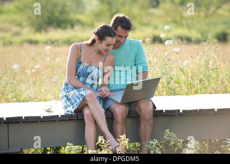 Couple sitting on countryside boardwalk with laptop computer Stock Photo