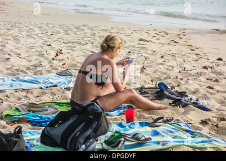 A Caucasian woman in her early 30s plays with her cell phone while sitting on Sandcastle Beach in St. Croix, U.S. Virgin Islands Stock Photo