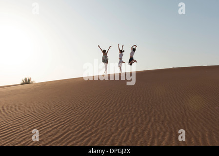 Children jumping on top of dune with arms raised in air Stock Photo