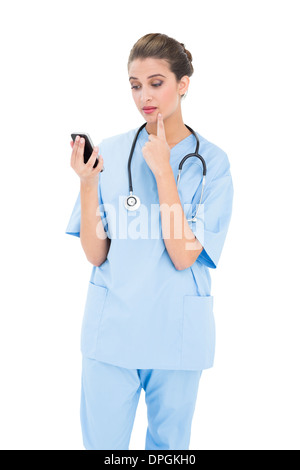 Troubled brown haired nurse in blue scrubs using a mobile phone Stock Photo