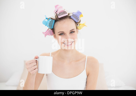 Amused natural brown haired woman in hair curlers holding a mug of coffee Stock Photo