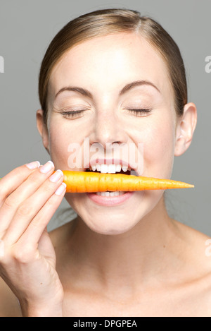 Young woman biting into carrot, eyes closed Stock Photo