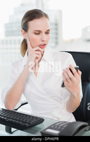Thoughtful businesswoman sitting at desk sending a text Stock Photo