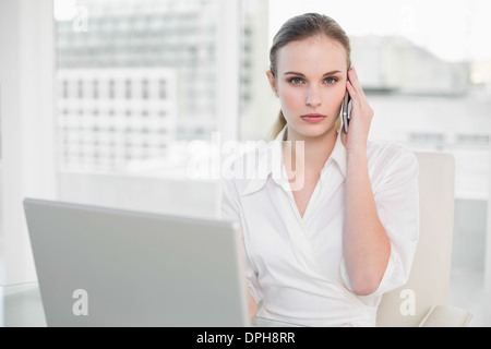 Frowning businesswoman using laptop and making a call Stock Photo