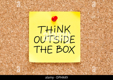 Think Outside The Box written on an yellow sticky note pinned on a cork bulletin board. Stock Photo