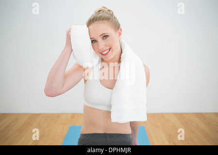 Smiling sporty blonde touching forehead with towel Stock Photo