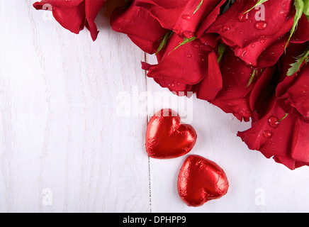 Red roses and two red chocolate hearts on light background Stock Photo