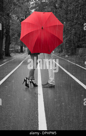 A Valentine's day black and white image of a young couple in the rain with a red umbrella. Stock Photo