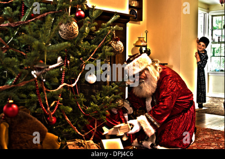 A little boy seeing Santa Claus putting presents under the Christmas Tree Stock Photo