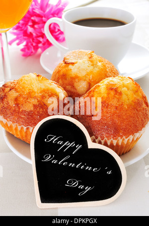 a continental breakfast with muffins, coffee and juice and the sentence happy valentines day written in a heart-shaped blackboar Stock Photo