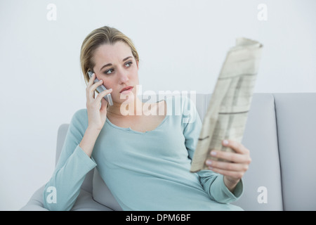 Casual thinking woman phoning while sitting on couch Stock Photo