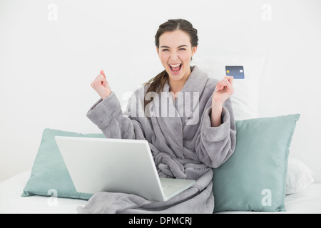 Excited woman in bathrobe doing online shopping in bed Stock Photo