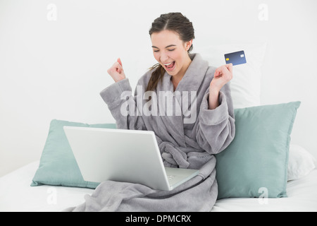 Excited woman in bathrobe doing online shopping in bed Stock Photo