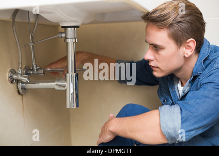 Handsome plumber repairing washbasin drain in bathroom Stock Photo