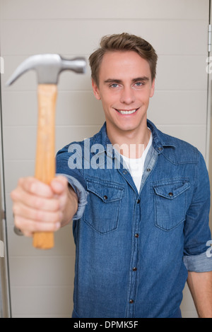 Smiling young handyman holding out hammer Stock Photo