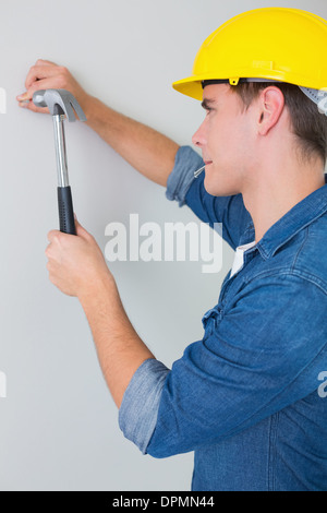 Side view of handyman hammering nail in wall Stock Photo