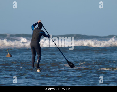 Stand up paddle boarder heading towards the waves, Bude, Cornwall, UK Stock Photo