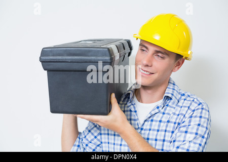Smiling handyman in yellow hard hat carrying toolbox Stock Photo