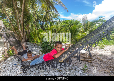 Young local boys lie in a hammock on a beach in Kosrae, Micronesia. Stock Photo
