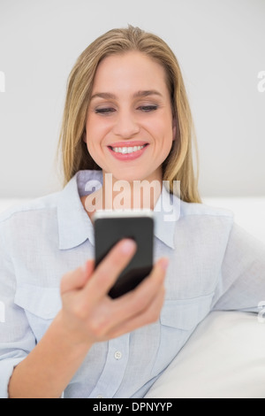 Laughing casual blonde relaxing on couch holding smartphone Stock Photo