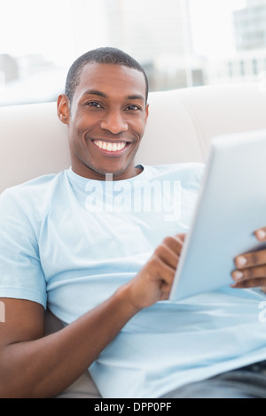 Casual smiling young Afro man using digital tablet on sofa Stock Photo