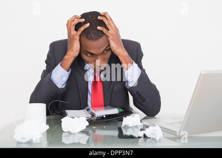 Frustrated Afro businessman with head in hands at desk Stock Photo