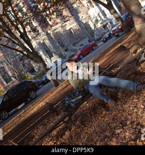 A man checks his phone while sitting on a bench on Commonwealth Avenue Mall in  Boston. Stock Photo