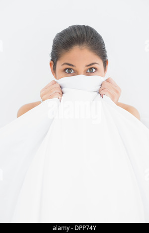 Portrait of a woman covering face with bedsheet in bed Stock Photo
