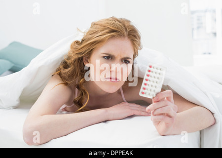 Young woman looking at pills in bed Stock Photo