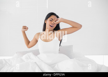 Cute dark haired woman stretching out while sitting on her bed Stock Photo