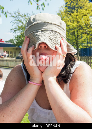 A woman pulls her hat over her eyes and sticks a tongue out at a photographer to stop him taking a photograph. Stock Photo