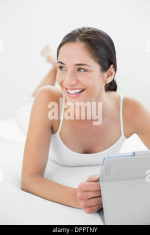 Smiling casual woman with tablet PC looks away in bed Stock Photo