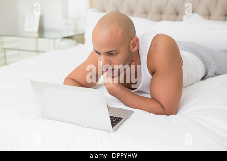 Casual bald man using laptop in bed Stock Photo