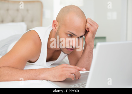 Serious casual bald young man using laptop in bed Stock Photo