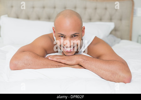 Smiling casual bald young man lying in bed Stock Photo