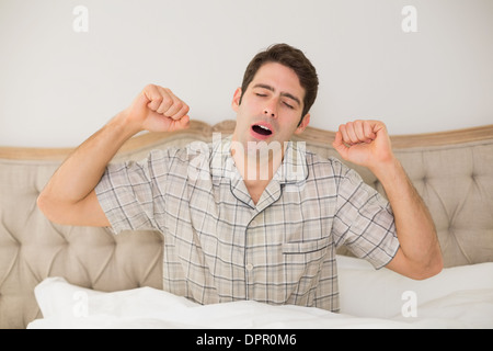 Young man waking up in bed and stretching his arms Stock Photo