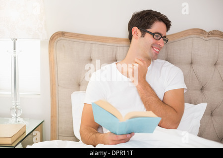Smiling relaxed man reading book in bed Stock Photo