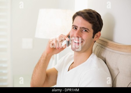 Casual smiling man using cellphone in bed Stock Photo