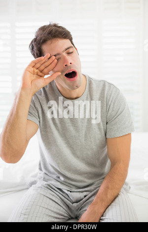 Sleepy man yawning as he rubs his eye in bed Stock Photo