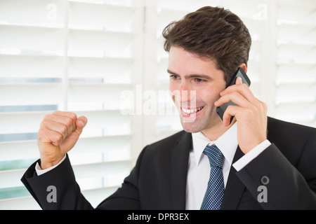 Smiling businessman using mobile phone while clenching fist Stock Photo