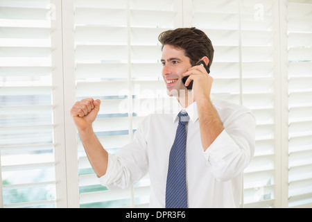 Smiling businessman using mobile phone while clenching fist Stock Photo