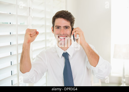 Smiling businessman using mobile phone while clenching fist Stock Photo