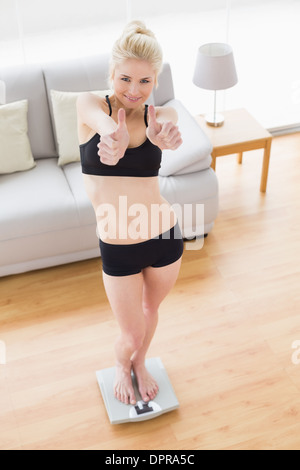 Woman in sportswear gesturing thumbs up on scale in fitness studio Stock Photo