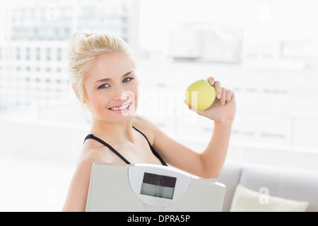 Fit woman holding scale and apple in fitness studio Stock Photo