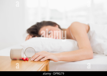 Woman in bed by spilt bottle of pills on table Stock Photo