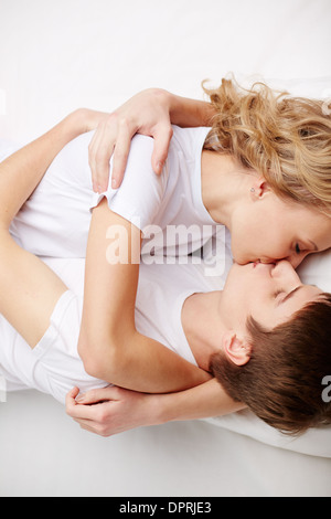 Two happy young dates lying in bed, embracing and kissing Stock Photo